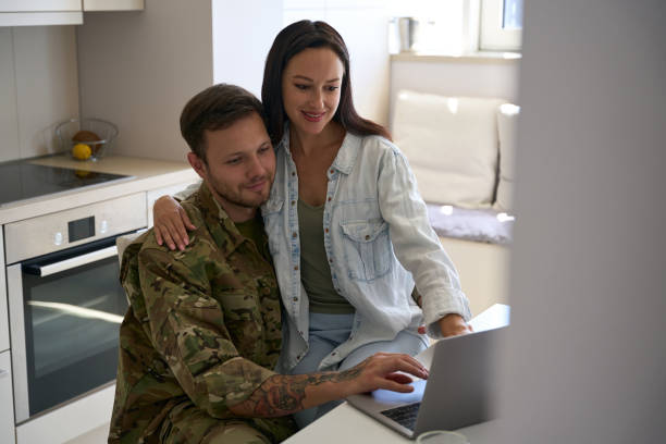 istock Wife sitting on soldier lap while using laptop in kitchen 1412206613
