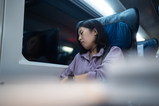 A young female tourist is sitting at the seat next to window and sleeping at night in a train.