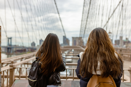 Two Asian tourist girls, students walking Brooklyn Bridge. Dumbo, Brooklyn, New York