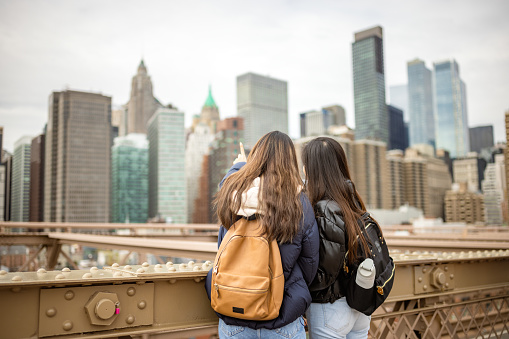 Two Asian tourist girls, students walking Brooklyn Bridge. They are taking selfie for a memory. Dumbo, Brooklyn, New York