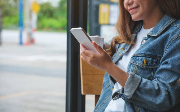 istock Closeup image of a young woman holding and using mobile phone while drinking coffee in cafe 1412209889