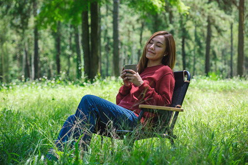 Portrait image of a beautiful young asian woman drinking coffee while sitting on a chair in the park