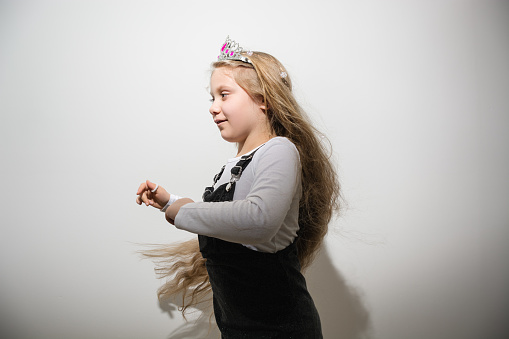 Girl with long blond loose hair and a pink crown on her head is spinning with joy against a gray wall. Child celebrates Christmas. Happy Birthday. Soft Selective focus. Copy Space for text.