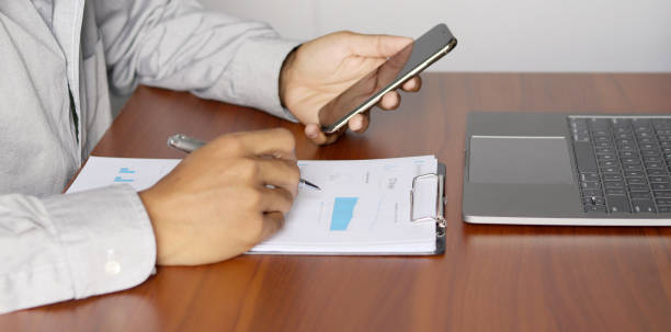 istock Businessman using laptop while holding smartphone to analyze graphs and charts on the office desk. Analysis of financial accounting strategies 1412212307