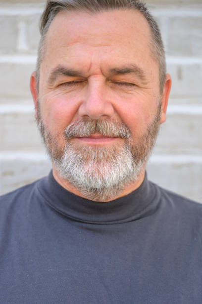 Senior man taking a moment to relax with closed eyes and a serene expression in a cropped close up portrait