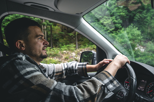 A man driving a car rides in a mountainous forest area, a view from inside the car.