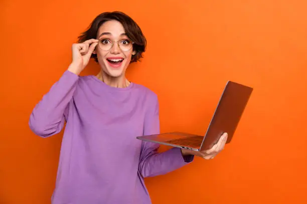 Photo of pretty impressed girl dressed purple pullover eyewear working modern gadget isolated orange color background.