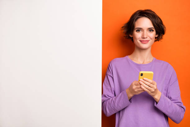 istock Photo of sweet pretty girl dressed purple pullover typing device white placard empty space isolated orange color background 1412214271