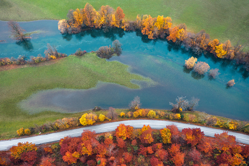 Aerial view on idyllic country road by the river. Mixed forest in autumn colours.