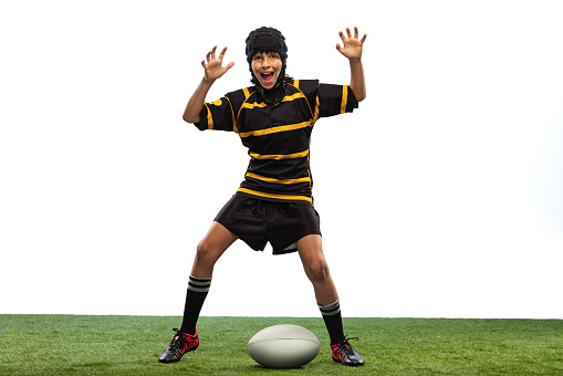 Having fun. One sportive boy, kid, male rugby player training with ball isolated on white background with grass floooring. Sport, team, studying, skills concept