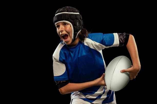 dynamisches porträt eines jungen im schulpflichtigen alter, eines männlichen rugbyspielers, der rugby-fußball praktiziert, isoliert auf dunklem hintergrund mit rasenfloooring. - rugby shirt stock-fotos und bilder