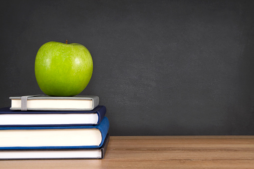 Stack of books with fresh green apple in front of chalkboard