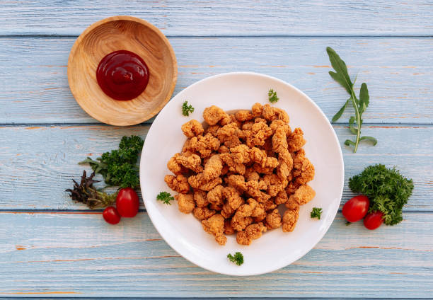 Homemade Crispy Popcorn Chicken in white plate with tomato ketchup and bbq sauce isolated on wooden table background top view fast food stock photo