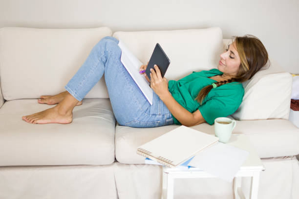 istock Beautiful woman lying down on sofa at home with books and doing homework 1412220961