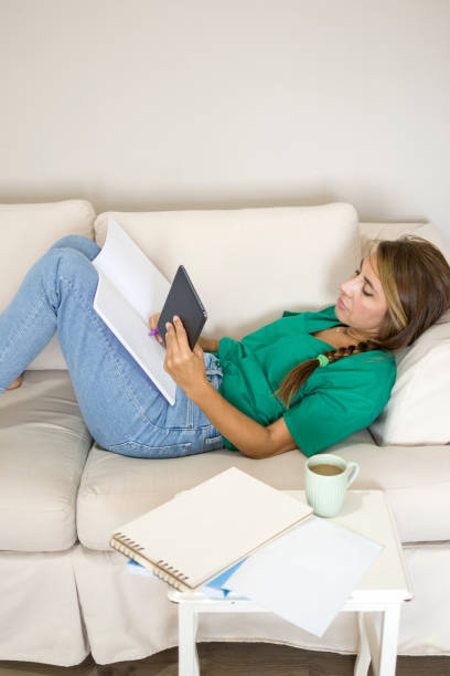 istock Beautiful woman lying down on sofa at home with books and doing homework 1412221253