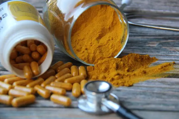 Turmeric powder and turmeric pills with a stethoscope on a wooden table, top view. Selective Focus. Turmeric (Curcuma longa), also known as turmeric, turmeric, sun root, turmeric, turmeric and yellow ginger, ginger family (Zingiberaceae).
