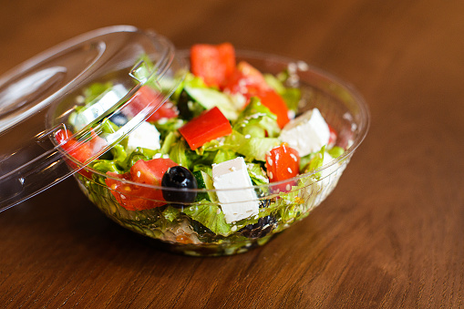 salad with feta cheese, olives and olive oil in plastic box on brown wooden background
