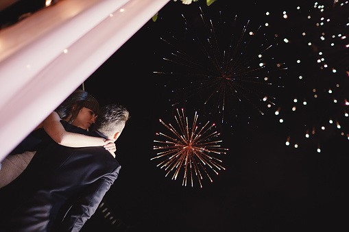 Happy hugging bride and groom watching beautiful colorful fireworks in the night sky. wedding day, party.