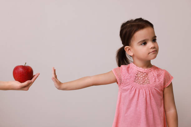 Cute little girl refusing to eat apple on grey background