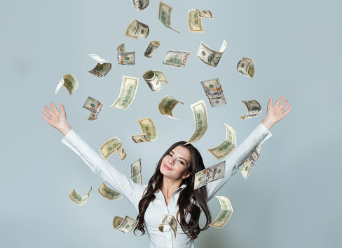 Happy smiling businesswoman with falling dollar cash money on grey background