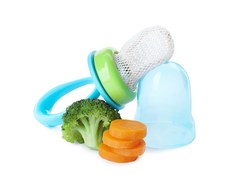 Empty nibbler with boiled broccoli and cut carrot on white background. Baby feeder