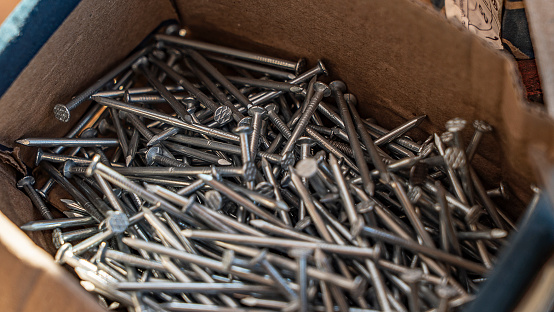 Nails pile in cardboard box close upper view. Metal fastening supplies. Construction site materials storage. Connecting wooden parts preparation