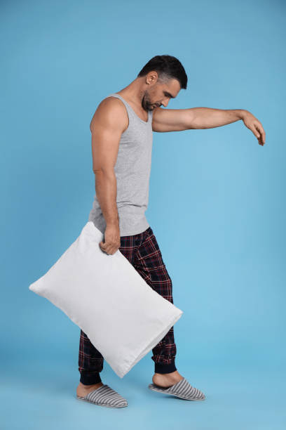istock Man with pillow in sleepwalking state on light blue background 1412226735