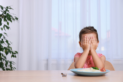 Cute little girl crying and refusing to eat her breakfast at home, space for text