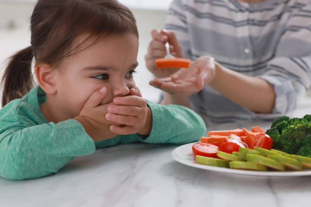 matka karmiąca córkę w pomieszczeniu, zbliżenie. mała dziewczynka odmawia jedzenia warzyw - cute disgust carrot caucasian zdjęcia i obrazy z banku zdjęć