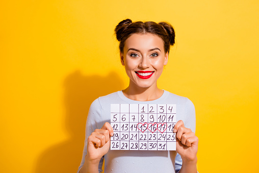 Photo of cheerful sweet lady wear long sleeve looking showing calendar isolated yellow color background.