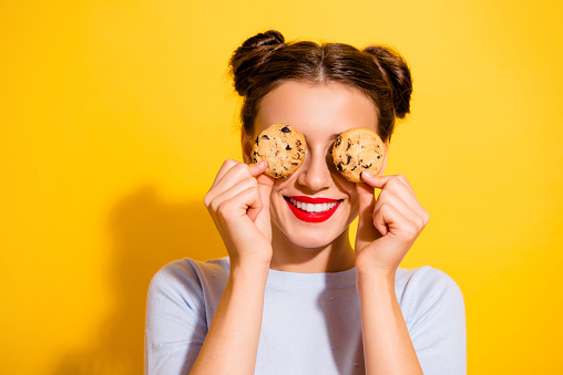 Photo of sweet pretty lady wear long sleeve holding two biscuits close eyes isolated yellow color background.