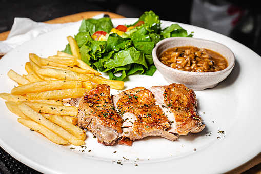 A white dish of chicken breast grilled with french fried and fresh dressing salad