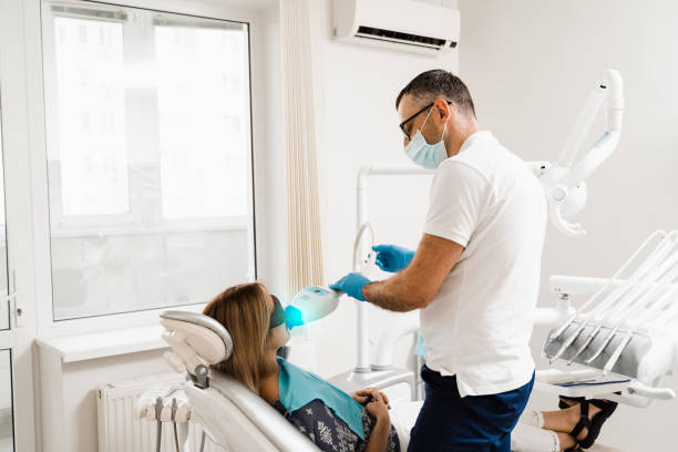 istock Artificial teeth whitening. Dental ultraviolet whitening treatment with light, fluoride and laser. Woman in red protective glasses patient do UV teeth whitening procedure. 1412232449