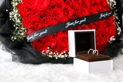 Pair of platinum wedding rings in a nice box in front of bouquet of red roses, romance, love and marriage concept