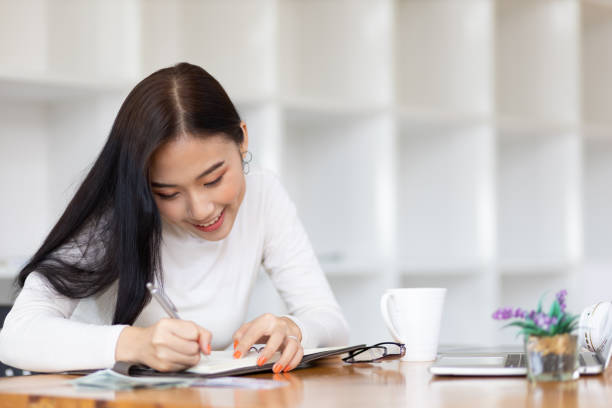 istock Beautiful Asian woman in the home office thinking and writing a schedule on a notepad. 1412233790