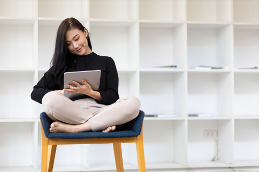 Attractive young Asian business woman wearing casual clothes is working on a tablet in the home office.