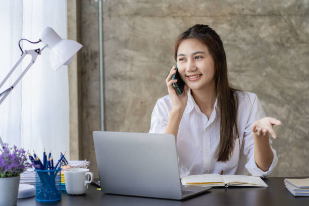 istock Business and communication concept, Asian woman working on laptop computer and reading smartphone on internet online at home, independent girl smiling using phone with social media. 1412236441