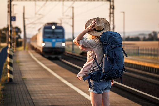 Woman backpacker with hat standing at railroad station and looking to arriving train