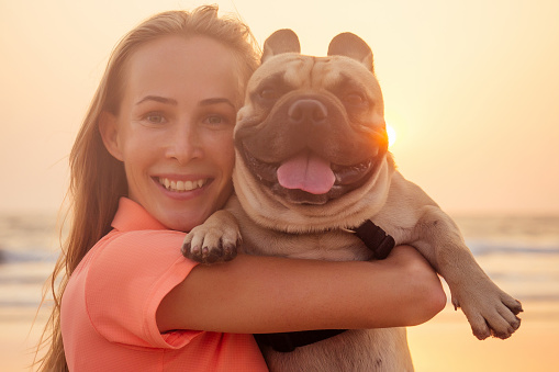 Happy blonde woman with french bulldog on india goa beach at sunset.