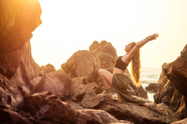 インディーのボヘミアンボーホースタイルの服のスタイリッシュな赤毛の栗の金髪の若い女の子黒スタイリッシュなtop.boho女性の長い髪、メイクアップと海沿いの岩の上でヨガのアーサナを� - yoga outdoors hippie people ストックフォトと画像