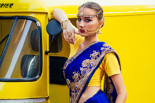 portrait indian beautiful Caucasian woman in traditional blue dress.hindu model with golden kundan jewelry set bindi earrings and nose ring piercing nath fashion photoshoot on srilankan street market