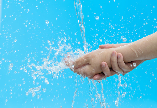Woman washing hands under flowing water on blue background.