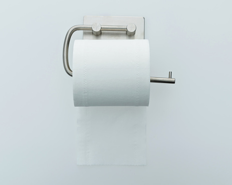 Roll of white toilet paper hanging on white background.