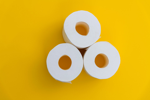 Three rolls of white toilet paper on yellow background.