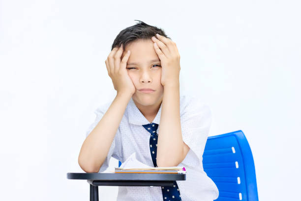 Excited little boy sitting at desk in classroom and holding up notebook with ruler. Adorable child being silly on lesson at school