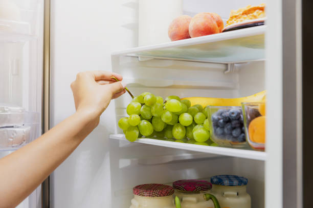 woman hand taking or picks up bunch of grapes out of open refrigerator or fridge - human hand gripping bottle holding imagens e fotografias de stock