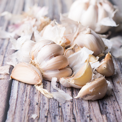 close-up of garlic cloves with skin scattered on wooden surface, antibacterial and antiseptic herb, soft-focus background with copy space