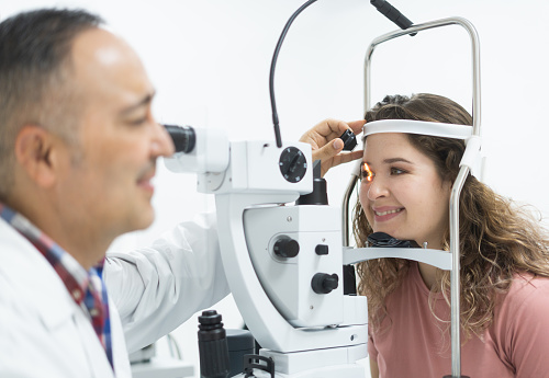 A latin woman sitting and smiling during an eye exam with a male ophthalmologist.