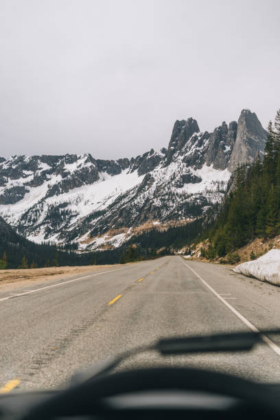 POV through vehicle to road and snowcapped mountains Targhee National Forest single yellow line sunlight usa utah stock pictures, royalty-free photos & images