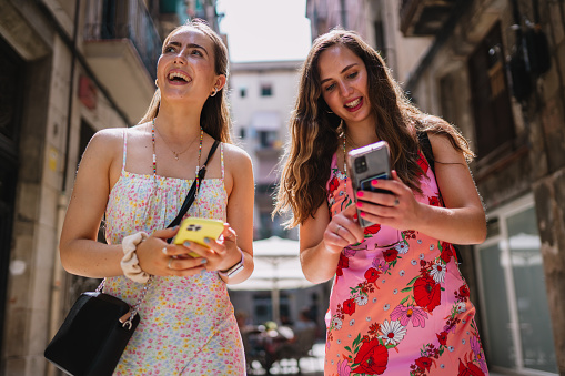 Happy female tourists phone users walking in old town alley an using smartphone. GPS maps, concept. Barcelona, Spain.
